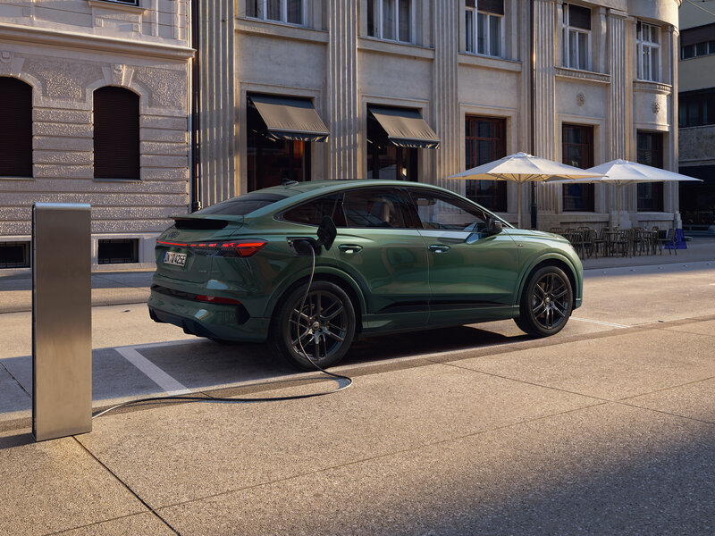 Audi Q4 Sportback e-tron in Grün steht seitlich an Ladesäule auf Parkplatz vor historischer Gebäudezeile mit Außengastronomie