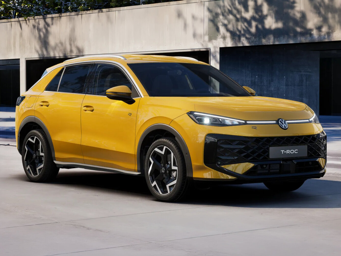 Volkswagen T-Roc in gelber Lackierung aus Front-Perspektive vor moderner Gebäudearchitektur auf befestigter Fläche geparkt