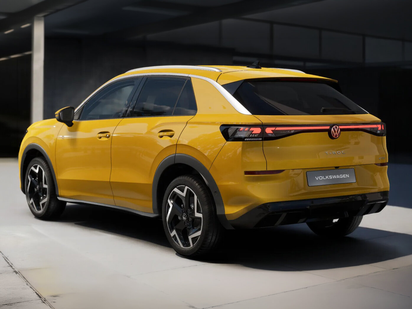 Volkswagen T-Roc in gelber Lackierung aus Heck-Perspektive vor moderner Gebäudearchitektur auf befestigter Fläche geparkt