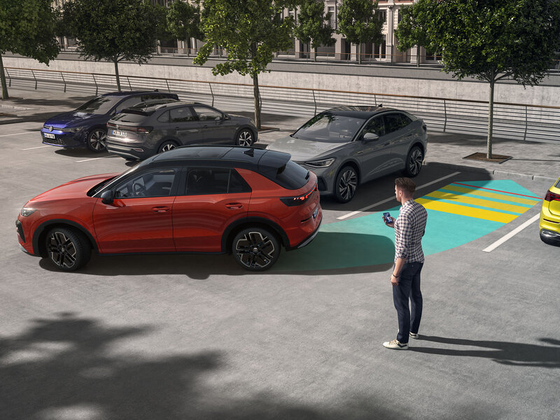 Ein Volkswagen T-Roc wird mithilfe grafisch dargestellter Assistenzsysteme in einer Parklücke manövriert, während eine Person daneben steht.