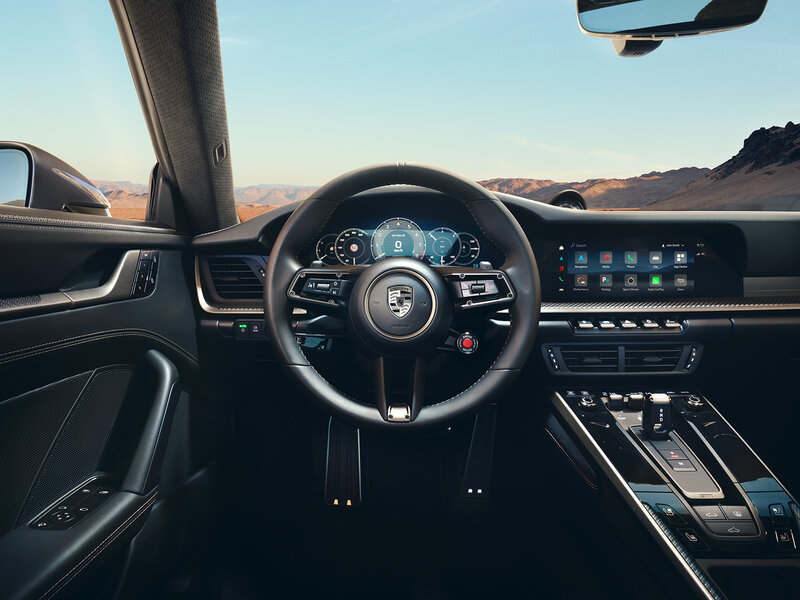 Innenansicht eines Porsche mit digitalem Cockpit, Lenkrad und zentralem Touchdisplay aus der Fahrerperspektive.
