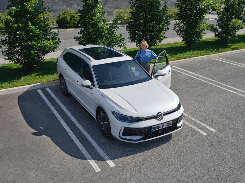 Ein weißer Volkswagen Passat Variant steht auf einem Parkplatz; eine Person öffnet die Fahrertür.