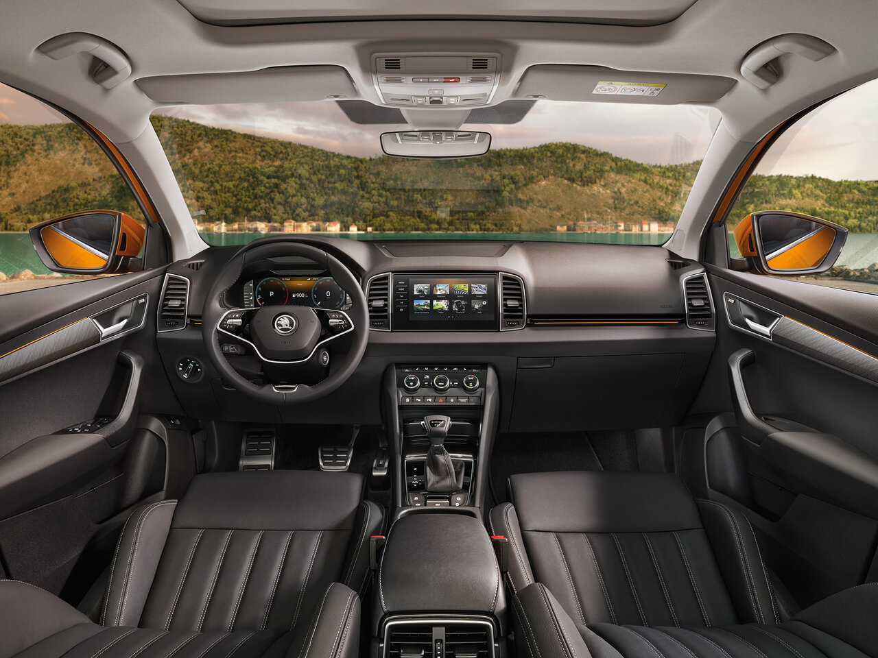 Cockpit des Škoda Karoq mit schwarzer Lederausstattung, zentralem Display und Blick durch die Frontscheibe auf eine Landschaft mit Hügeln.