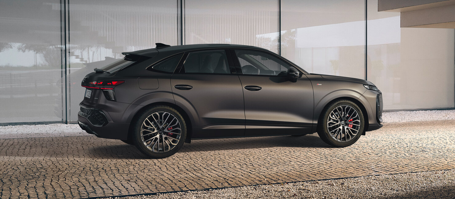 Audi Q3 Sportback in Seitenansicht, geparkt vor Glasfassade, sportliche Coupé-Dachlinie und große Leichtmetallräder