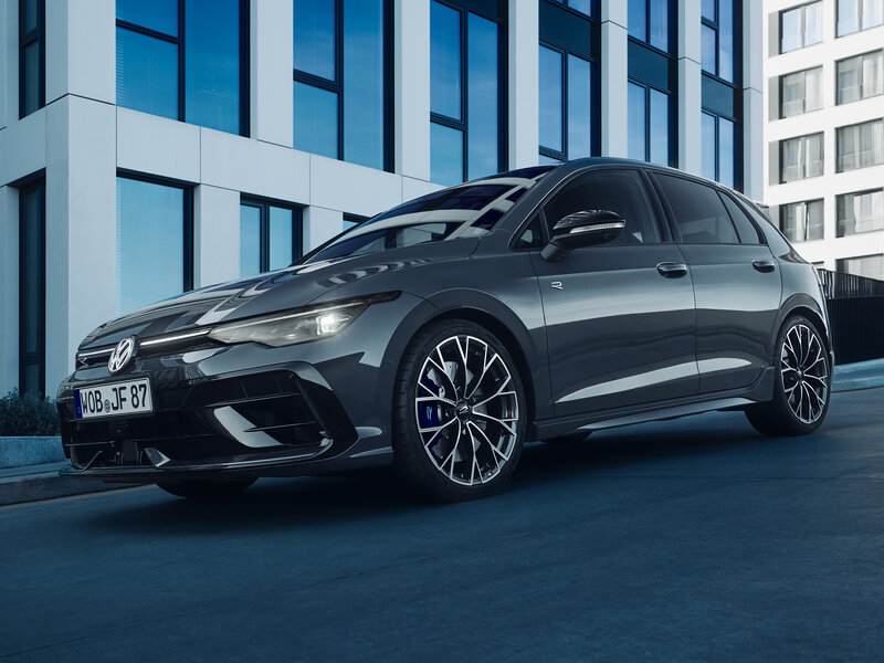 Ein grauer Volkswagen Golf R fährt durch eine moderne urbane Umgebung mit Glasfassaden.