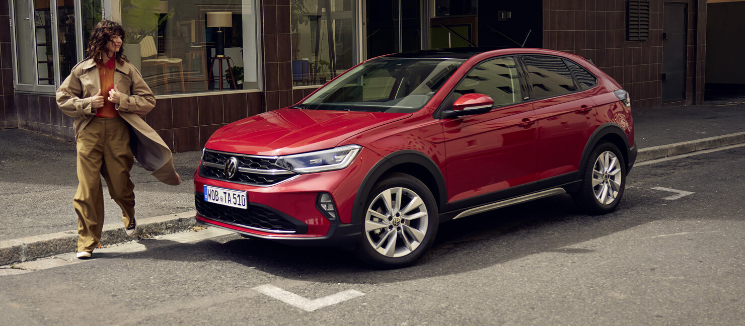 Roter Volkswagen Taigo parkt am Straßenrand, daneben geht eine Person vorbei, urbane Alltagsszene in der Stadt