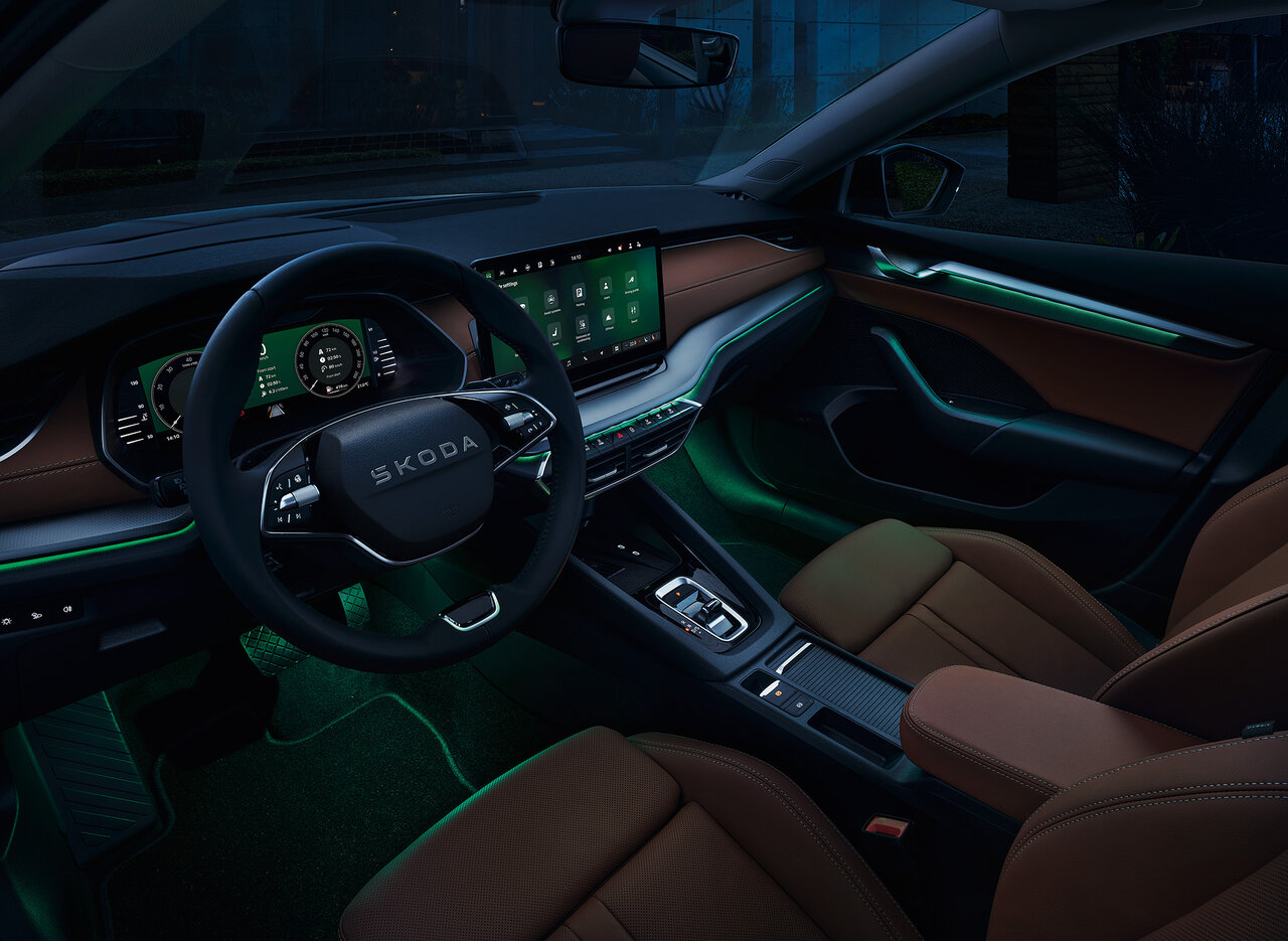 Innenraum des Škoda Octavia Combi mit braunen Sitzen, digitalem Display und grüner Ambientebeleuchtung bei Dunkelheit.