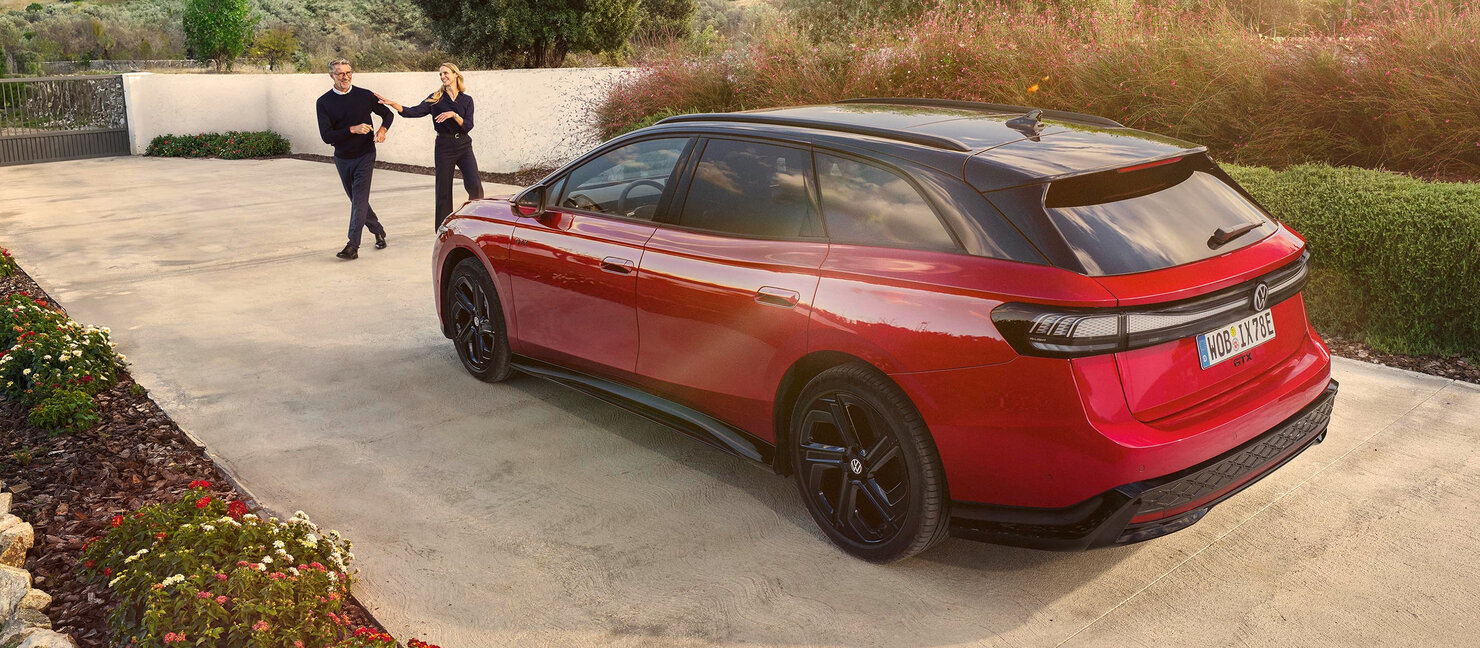 Roter VW ID.7 GTX Tourer steht auf einer Einfahrt, während zwei Personen lächelnd daran vorbeigehen