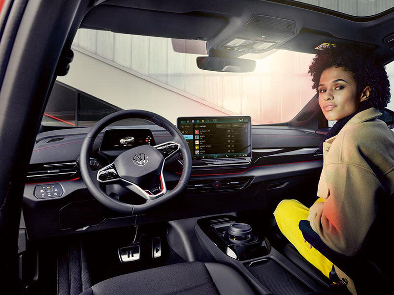 Innenraum des Volkswagen ID.4 GTX mit digitalem Cockpit, zentralem Touchdisplay und Multifunktionslenkrad, eine Person sitzt auf dem Beifahrersitz.