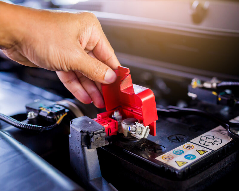Hand greift in den Motorraum um Batterie zu prüfen. 