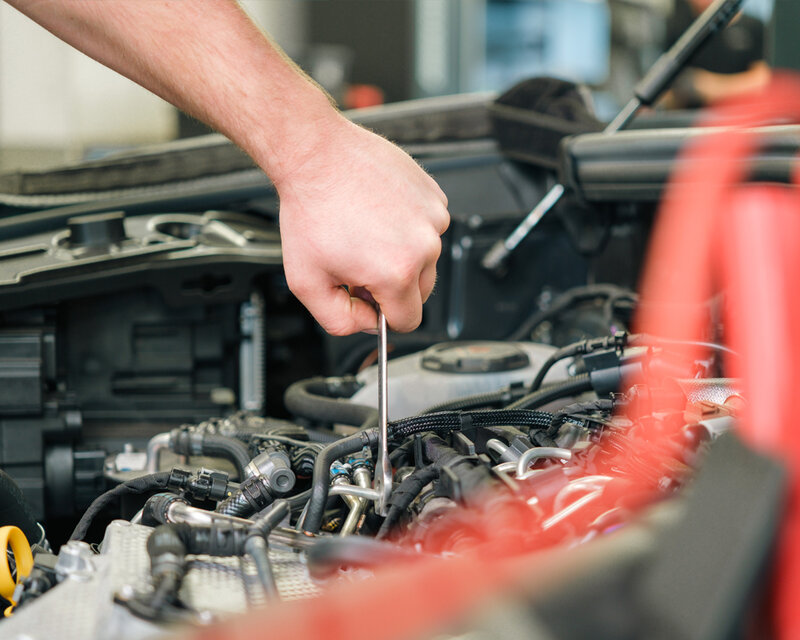 Kfz-Mechaniker arbeitet mit Schraubenschlüssel im Motorraum.