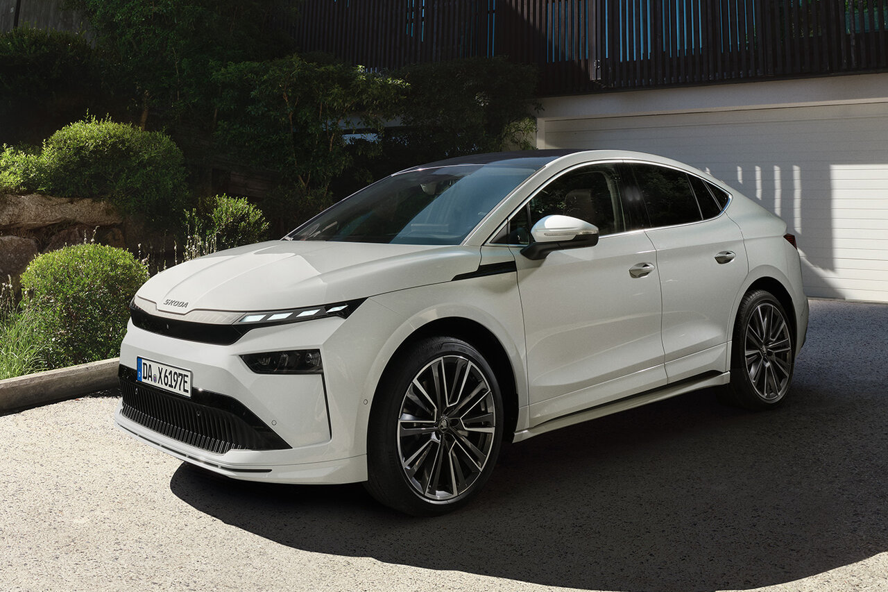 Škoda Enyaq Coupé in Weiß steht vor einem modernen Wohnhaus bei sonnigem Wetter.