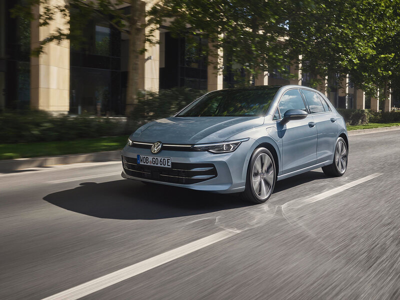 Volkswagen Golf GTE fährt auf einer städtischen Straße bei Tageslicht zwischen Bäumen und modernen Gebäuden
