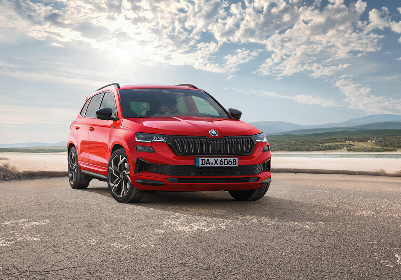 Škoda Karoq Sportline in Rot steht auf einer offenen Fläche mit Blick auf Berge und blauen Himmel.