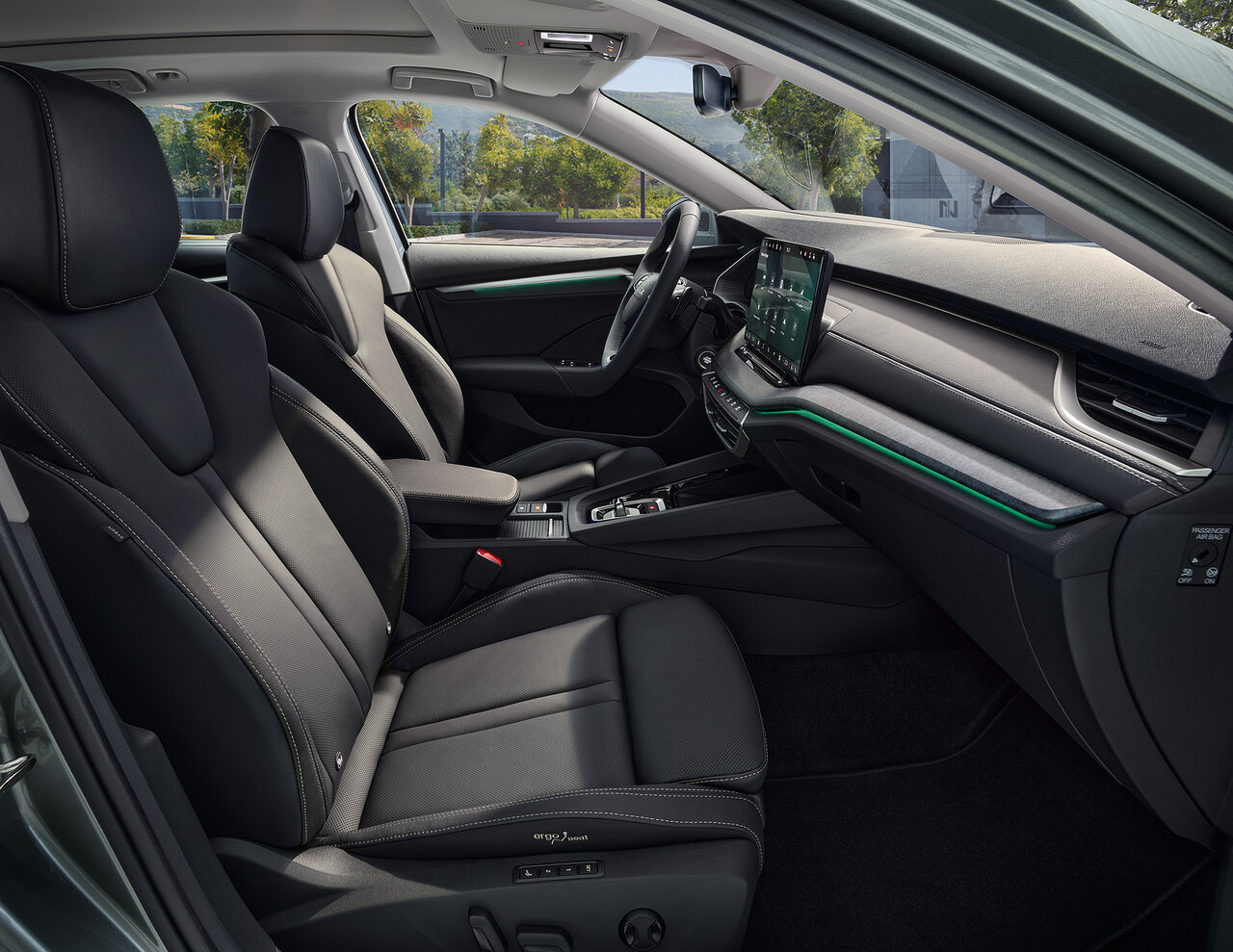 Innenraum des Škoda Octavia Combi mit schwarzen Sitzen, digitalem Display und grüner Ambientebeleuchtung bei Tageslicht.