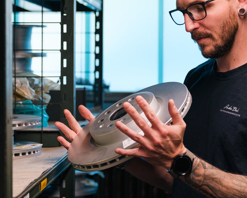 Teiledienstmitarbeiter hält Bremsscheibe in der Hand.
