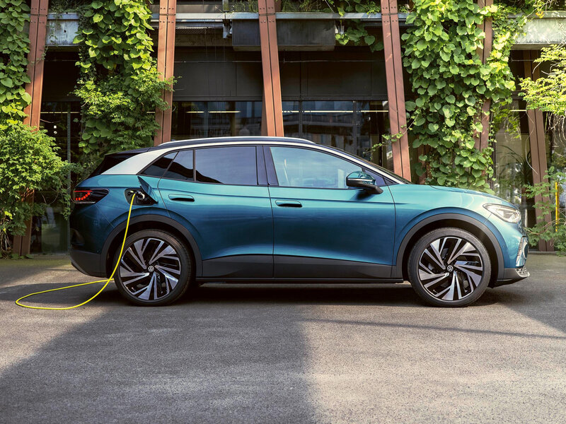 Volkswagen ID.4 steht seitlich vor einem Gebäude mit begrünten Fassaden und ist über ein Ladekabel an einer Wallbox angeschlossen.
