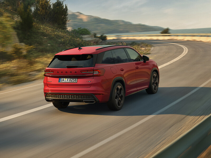 Škoda Kodiaq RS in Rot fährt auf kurvenreicher Straße entlang einer Berglandschaft mit Blick auf das Wasser.