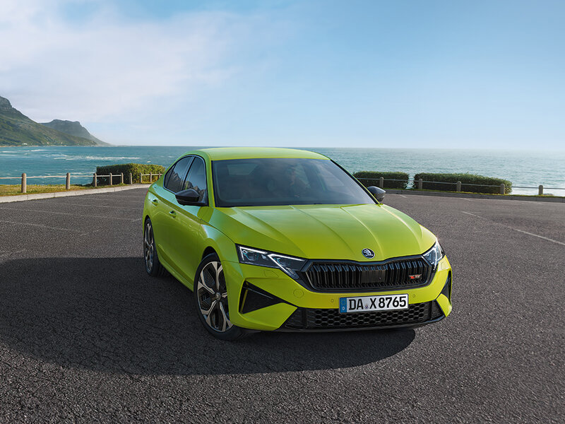 Škoda Octavia RS Limousine in Mamba-Grün steht auf einem Parkplatz mit Blick auf Meer und Berge bei sonnigem Wetter
