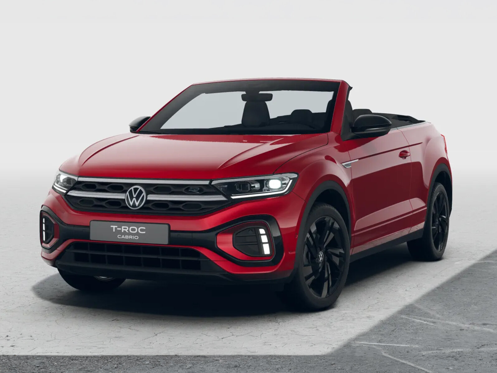 Rotes Volkswagen T-Roc Cabriolet mit geöffnetem Verdeck in schräger Frontansicht und schwarzen Felgen vor neutralem hellem Hintergrund