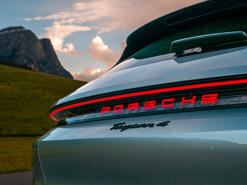 Rückansicht eines Porsche Taycan mit durchgehendem LED-Leuchtenband und beleuchtetem Porsche-Schriftzug.