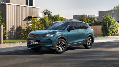 Volkswagen Tiguan Energy in Türkis fährt auf Wohnstraße vor moderner Wohnsiedlung bei Tageslicht