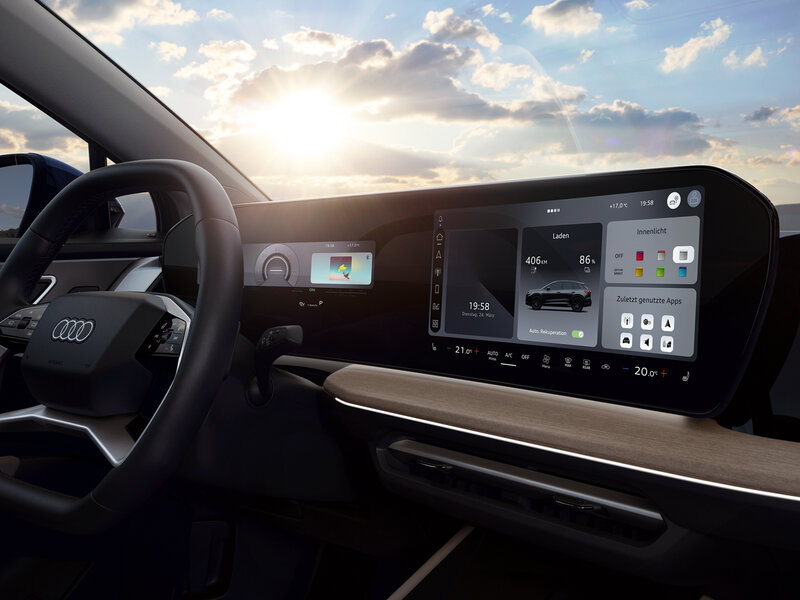 Cockpit eines Audi mit breitem Touchdisplay, Lenkrad und Sicht auf digitale Benutzeroberfläche bei Sonnenuntergang durch die Frontscheibe
