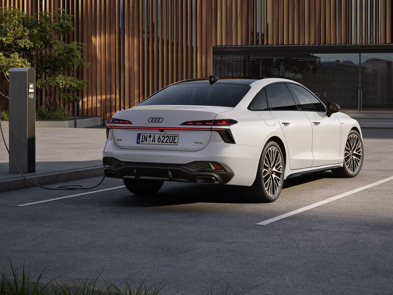 Audi A6 Limousine beim Laden an einer Wallbox, modernes Heckdesign vor urbaner Architektur mit Holzfassade