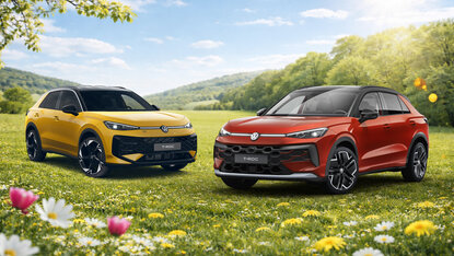 Zwei Volkswagen T-Roc in Gelb und Rot stehen nebeneinander auf einer blühenden Wiese vor hügeliger Landschaft bei Sonnenschein