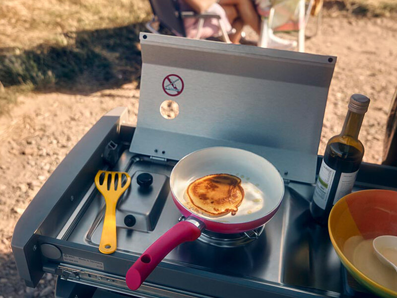 Ausziehbare Campingküche im Volkswagen Caddy California mit Gaskocher, Pfanne und Küchenutensilien im Freien aufgebaut.