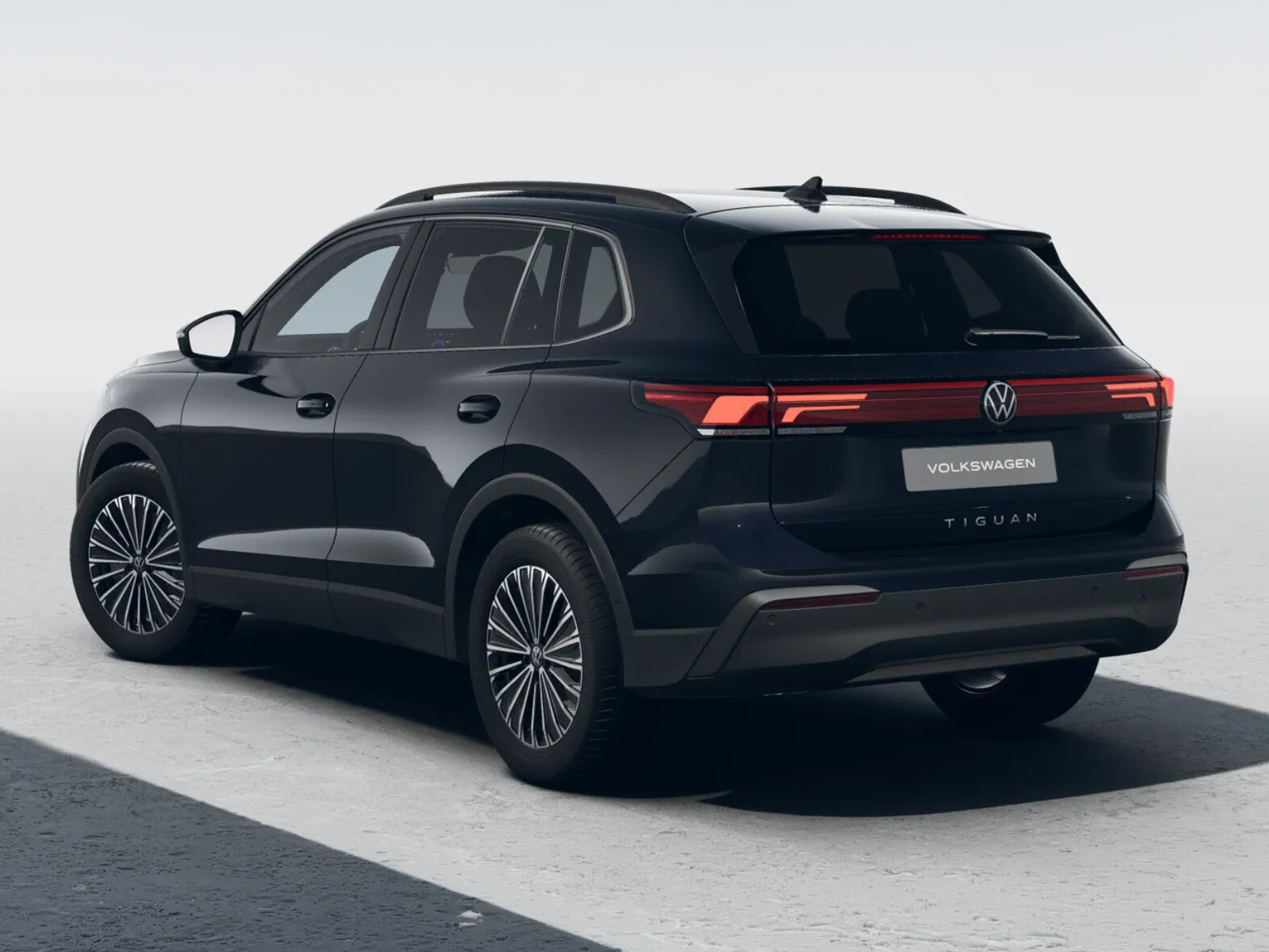 Schwarzer Volkswagen Tiguan in schräger Heckansicht mit durchgehendem Rücklicht vor neutralem hellem Hintergrund