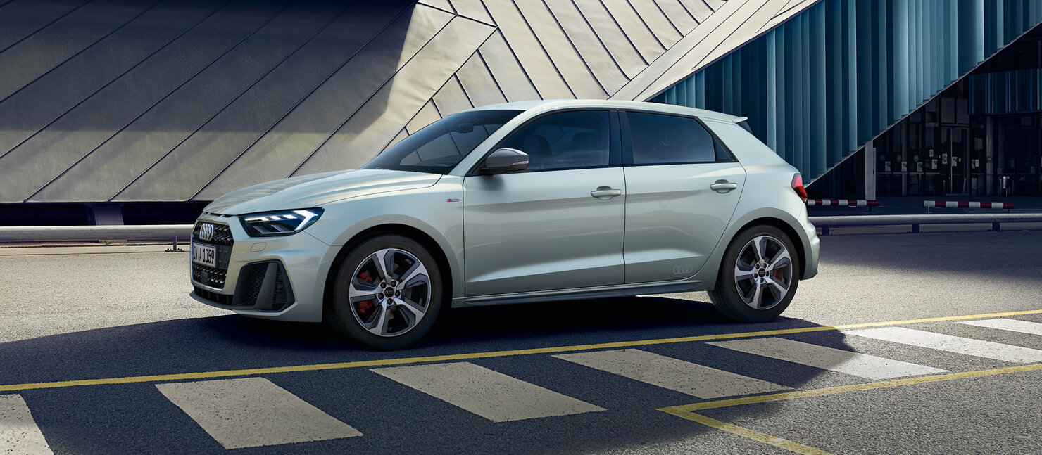 Audi A1 Sportback in Silber fährt durch urbane Umgebung und betont sportliche Proportionen und dynamische Linien