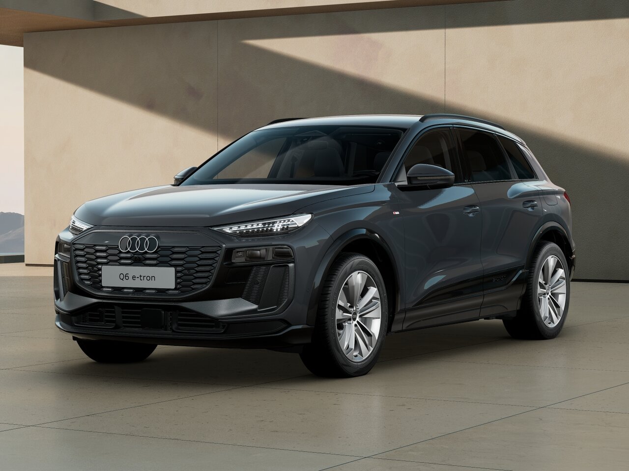 Audi Q6 e-tron in Frontansicht schräg von vorn vor moderner Architektur mit geschlossener Front, schmalen LED-Scheinwerfern und markantem Singleframe-Grill