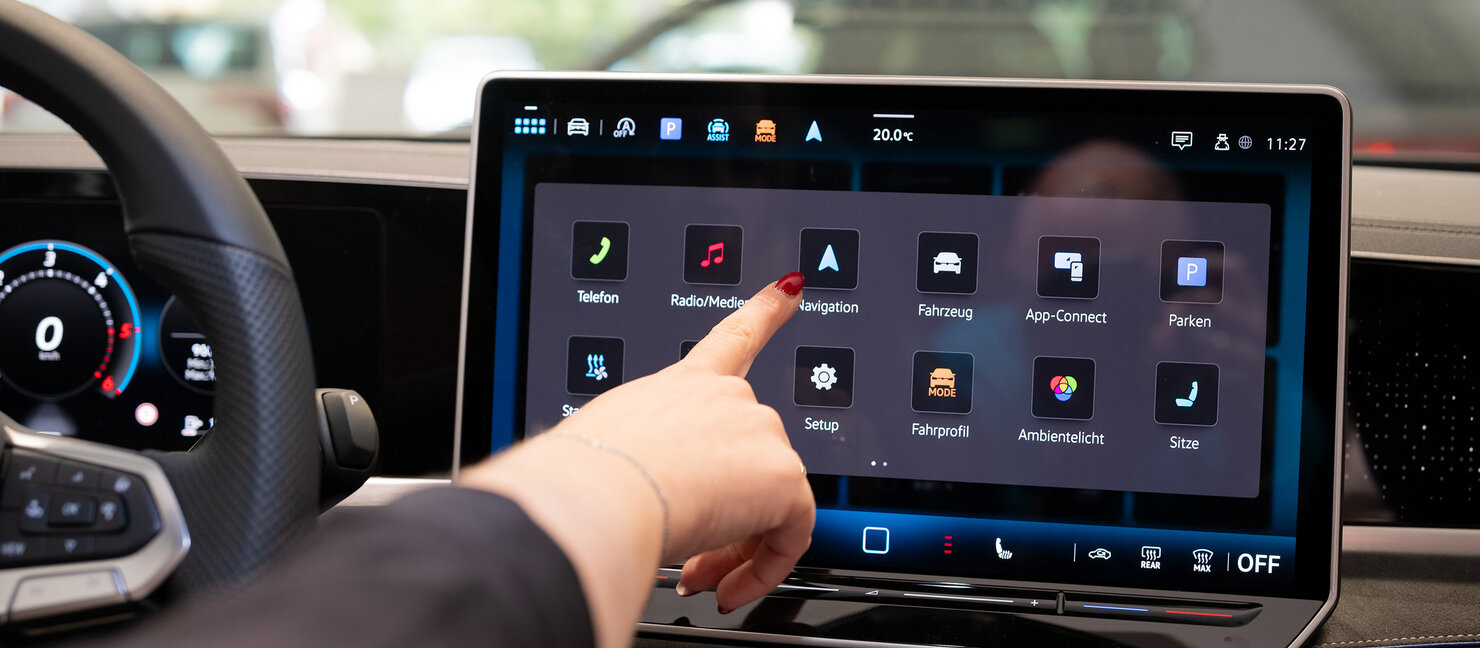 Hand bedient das zentrale Infotainment-Display eines Volkswagen Fahrzeugs im Auto Bach Autohaus