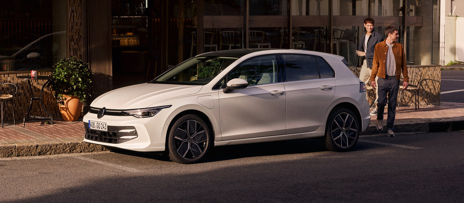 Volkswagen Golf in Weiß parkt vor einem Café in sonniger Stadtumgebung