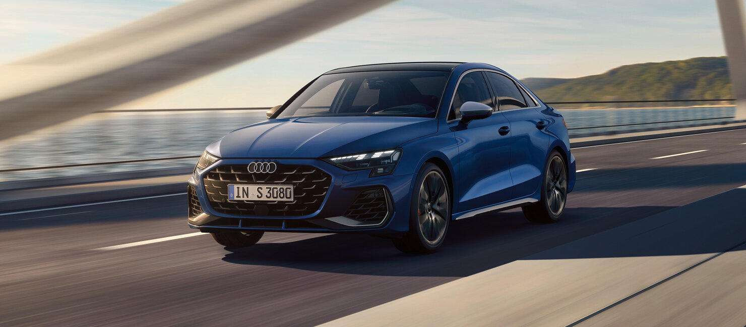 Blauer Audi S3 Limousine in Fahrt auf einer Brücke, seitlich-frontale Perspektive mit Fokus auf Design und Dynamik