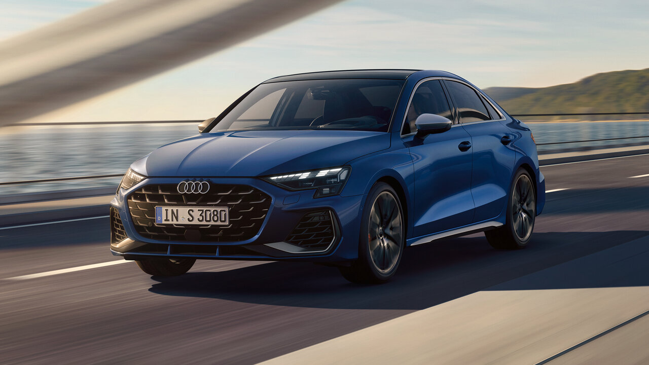 Blauer Audi S3 Limousine fährt dynamisch über eine Brücke, Frontansicht mit markanter Lichtsignatur und sportlichem Auftritt