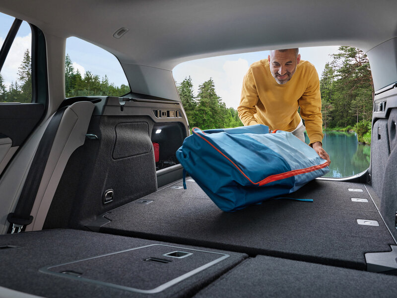 Blick in den offenen Kofferraum eines Volkswagen Passat Variant mit umgeklappter Rückbank, während eine Person ein Gepäckstück einlädt.