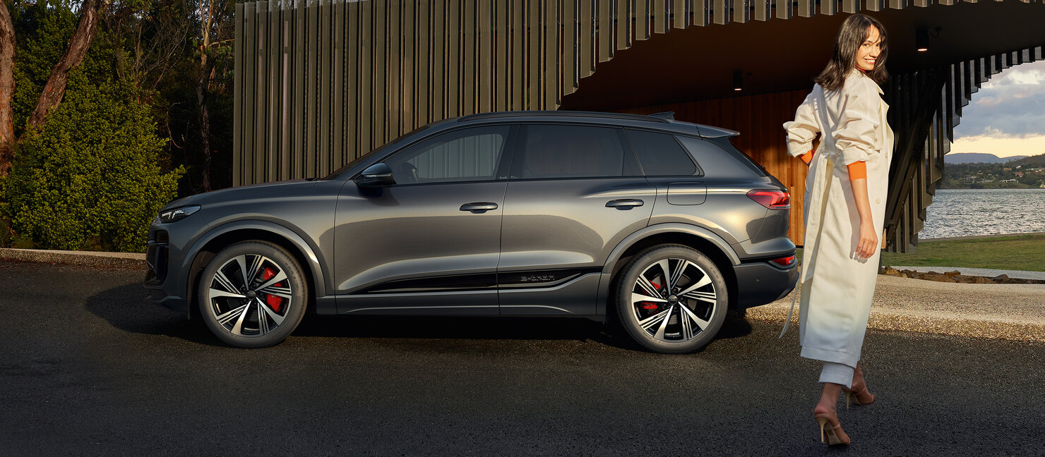 Audi SQ6 e-tron in Seitenansicht, parkend vor modernem Gebäude, daneben eine Person auf dem Gehweg