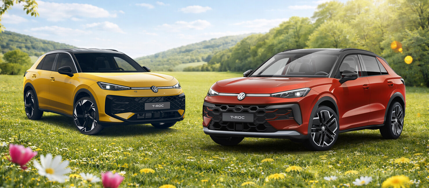 Zwei Volkswagen T-Roc in Gelb und Rot stehen nebeneinander auf einer blühenden Wiese vor hügeliger Landschaft bei Sonnenschein