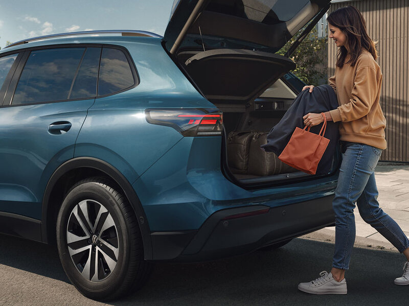Eine Person lädt Gepäck in den offenen Kofferraum eines Volkswagen Tiguan.
