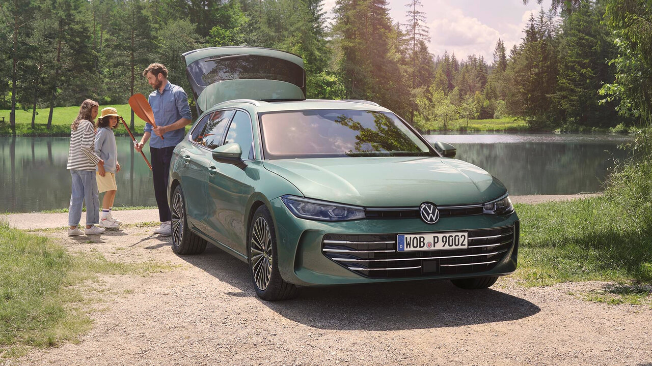 Grüner Volkswagen Passat steht mit geöffneter Heckklappe an einem See, während eine Familie Gepäck einlädt