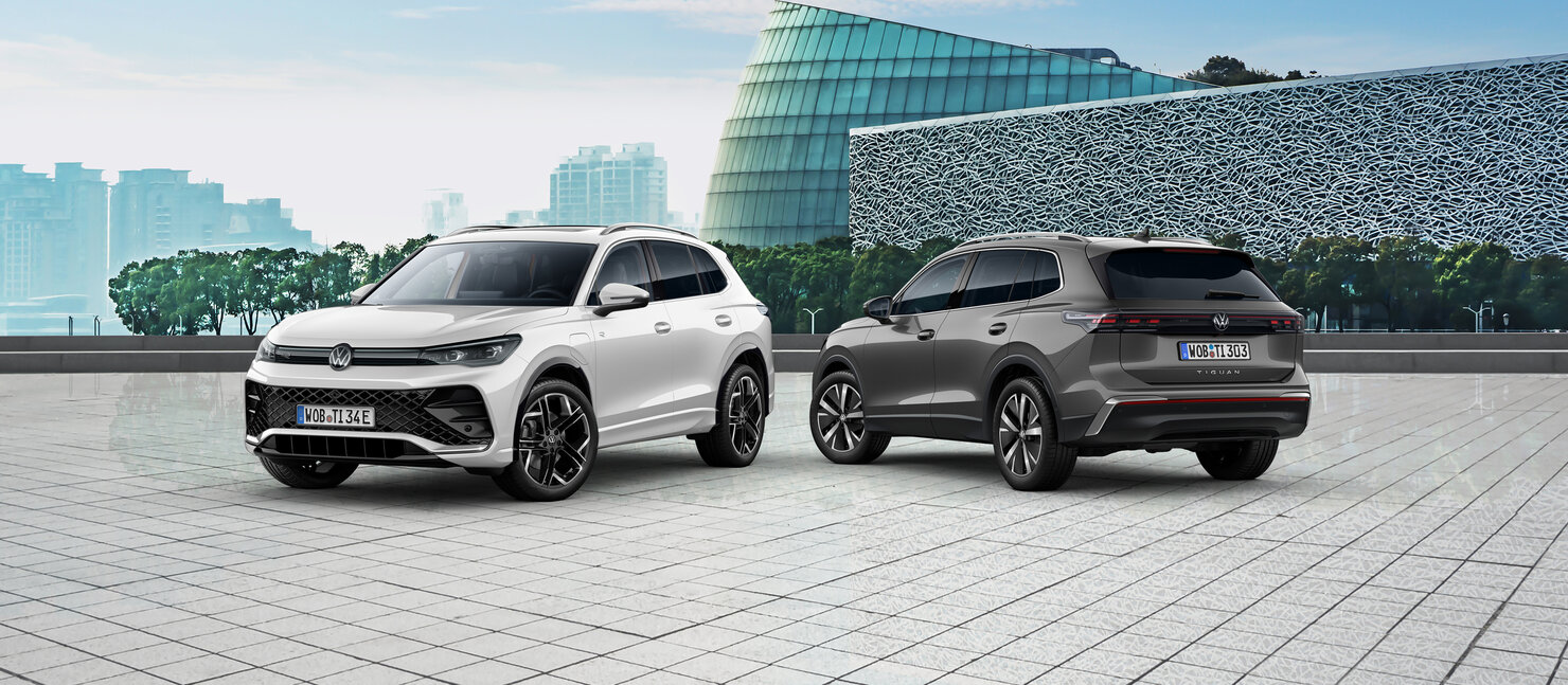 Zwei Volkswagen Tiguan stehen nebeneinander auf gepflastertem Platz vor moderner Architektur in urbaner Umgebung