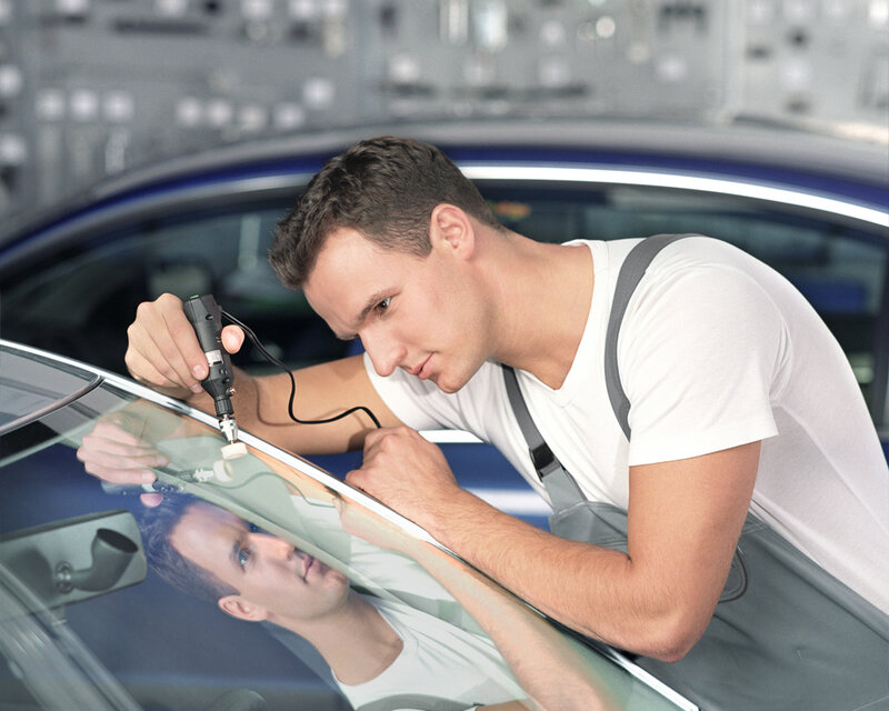 Kfz-Mitarbeiter repariert Steinschlag an der Windschutzscheibe mit Spezialwerkzeug in der Werkstatt.