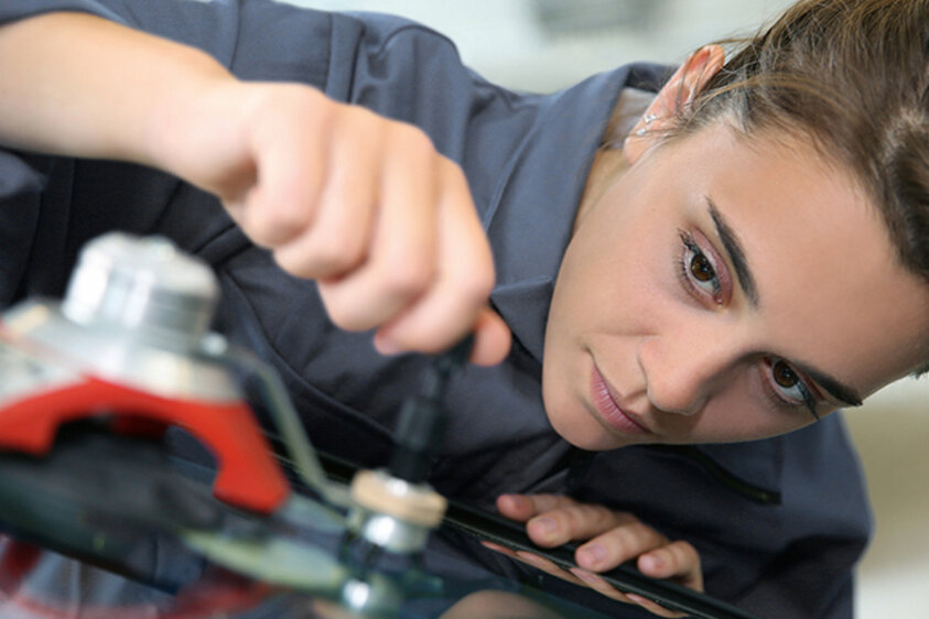 Werkstattmitarbeiterin repariert einen Steinschlagschaden an einer Autoscheibe mit Spezialwerkzeug