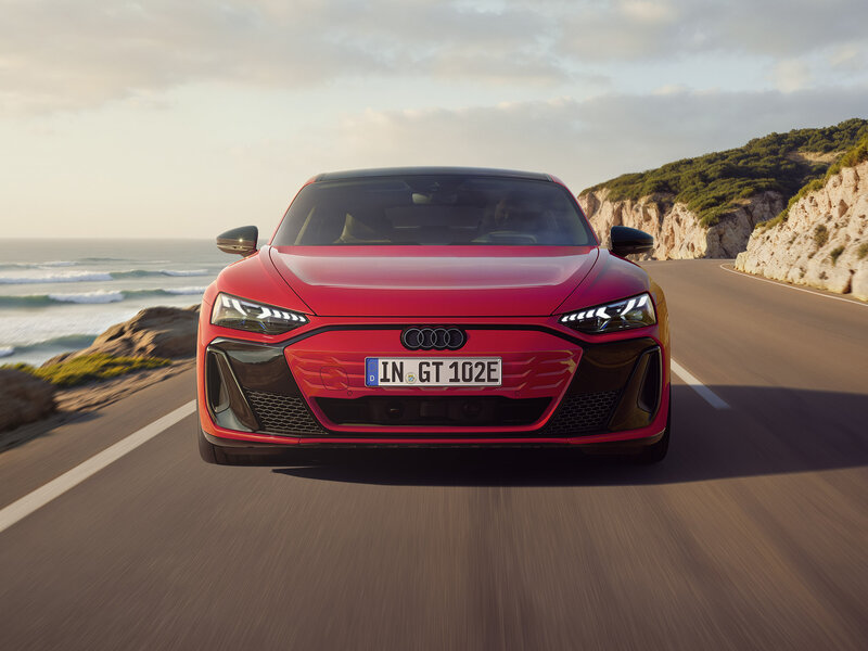 Audi e-tron GT quattro fährt dynamisch auf Küstenstraße, Frontansicht mit flacher GT-Silhouette
