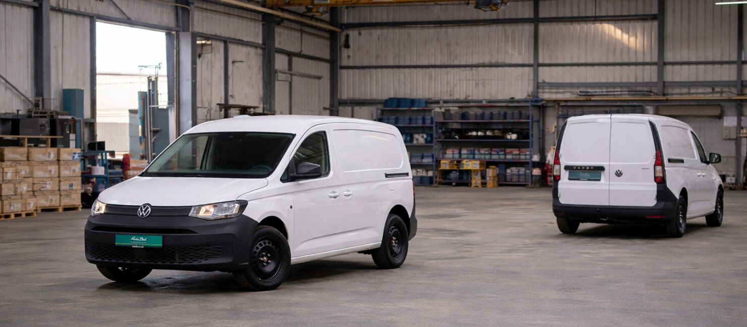 Zwei Volkswagen Caddy Kastenwagen in Front- und Heckansicht stehen in einer Industriehalle mit Regalen, Paletten und Werkstattausstattung im Hintergrund