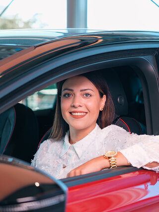 Frau sitzt im roten Fahrzeug im Autohaus Auto Bach und blickt aus dem geöffneten Seitenfenster