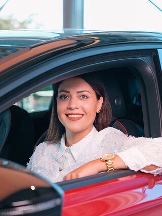 Frau sitzt im roten Fahrzeug im Autohaus Auto Bach und blickt aus dem geöffneten Seitenfenster