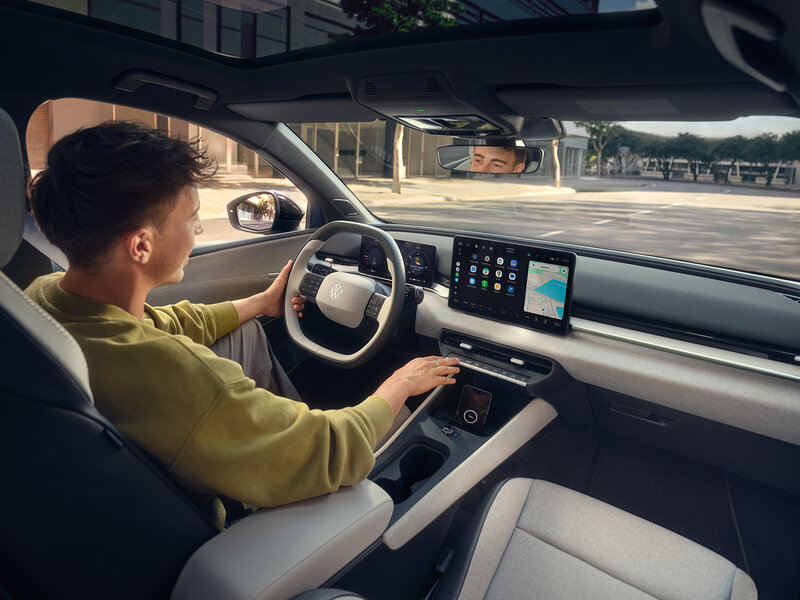 Innenraum des Volkswagen ID. Polo mit Fahrer am Lenkrad und Blick auf digitales Infotainment-Display während der Fahrt auf einer Straße